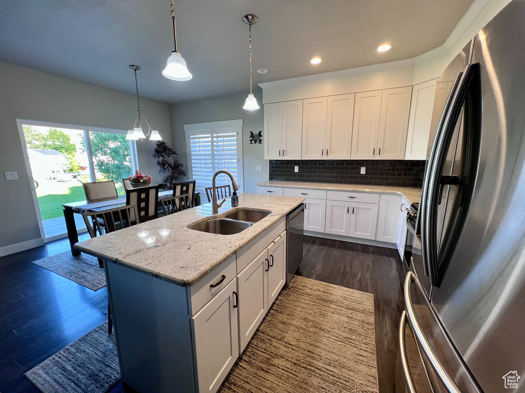 Kitchen featuring appliances with stainless steel finishes, dark wood-type flooring, white cabinetry, a center island with sink, and tasteful backsplash