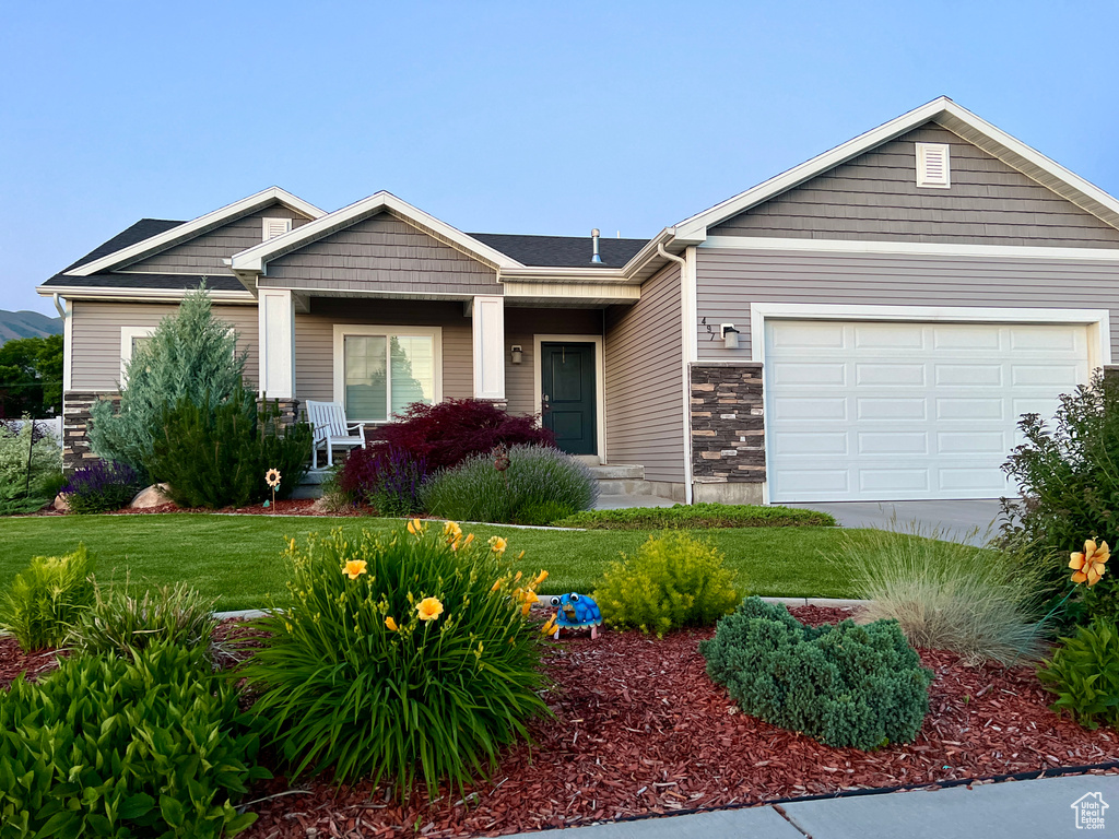 Craftsman inspired home with stone siding, a front yard, covered porch, a garage, and driveway
