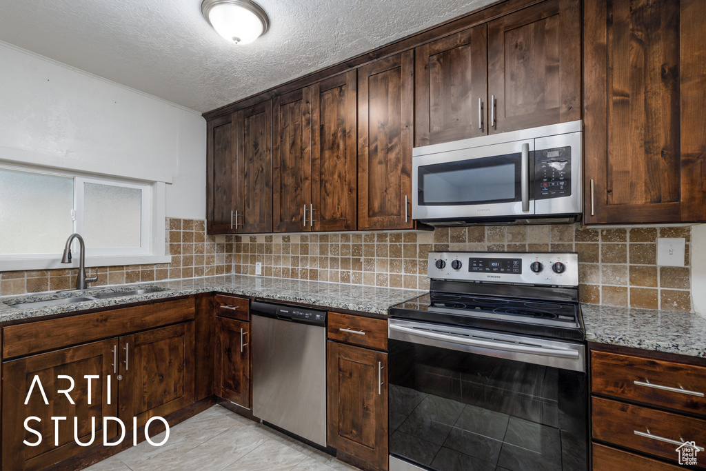 Kitchen featuring stainless steel appliances, light stone counters, backsplash, a textured ceiling, and dark brown cabinets