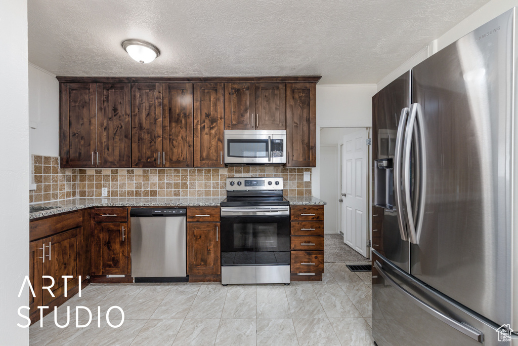 Kitchen with stainless steel appliances, a textured ceiling, decorative backsplash, and dark brown cabinets