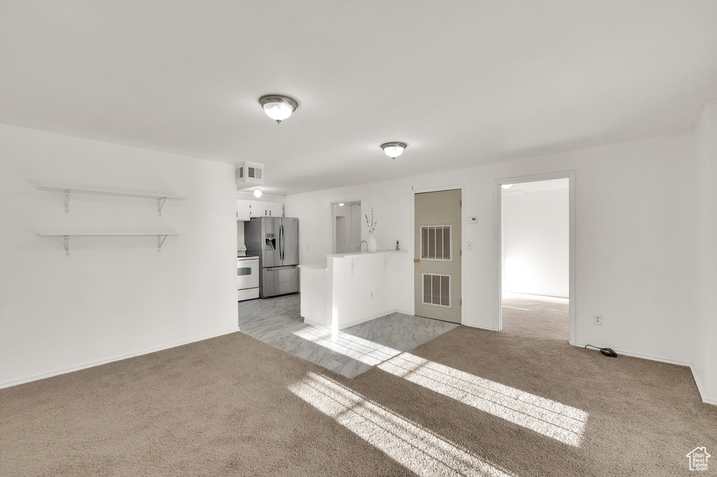 Unfurnished living room featuring light carpet and baseboards