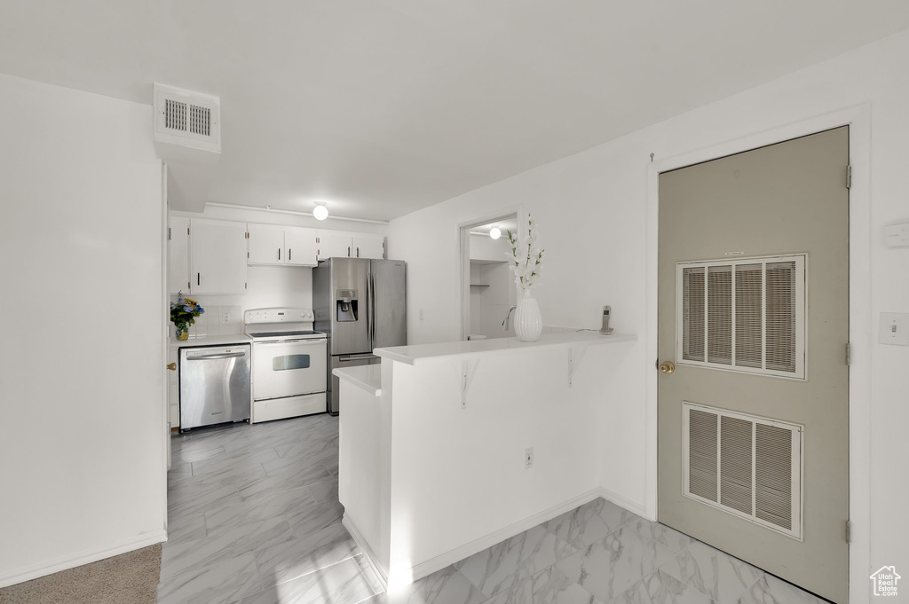 Kitchen featuring appliances with stainless steel finishes, a peninsula, light countertops, white cabinetry, and a kitchen bar