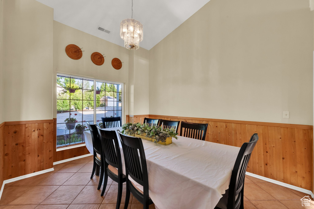 Tiled dining area featuring a wainscoted wall, high vaulted ceiling, a chandelier, and wood walls