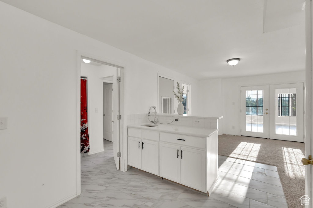 Kitchen with white cabinetry, light countertops, french doors, a peninsula, and light marble finish flooring