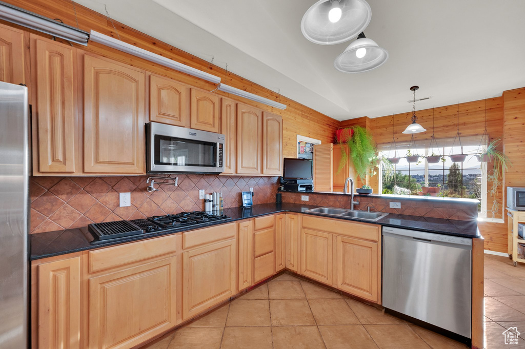 Kitchen featuring appliances with stainless steel finishes, light brown cabinetry, dark countertops, tasteful backsplash, and wood walls