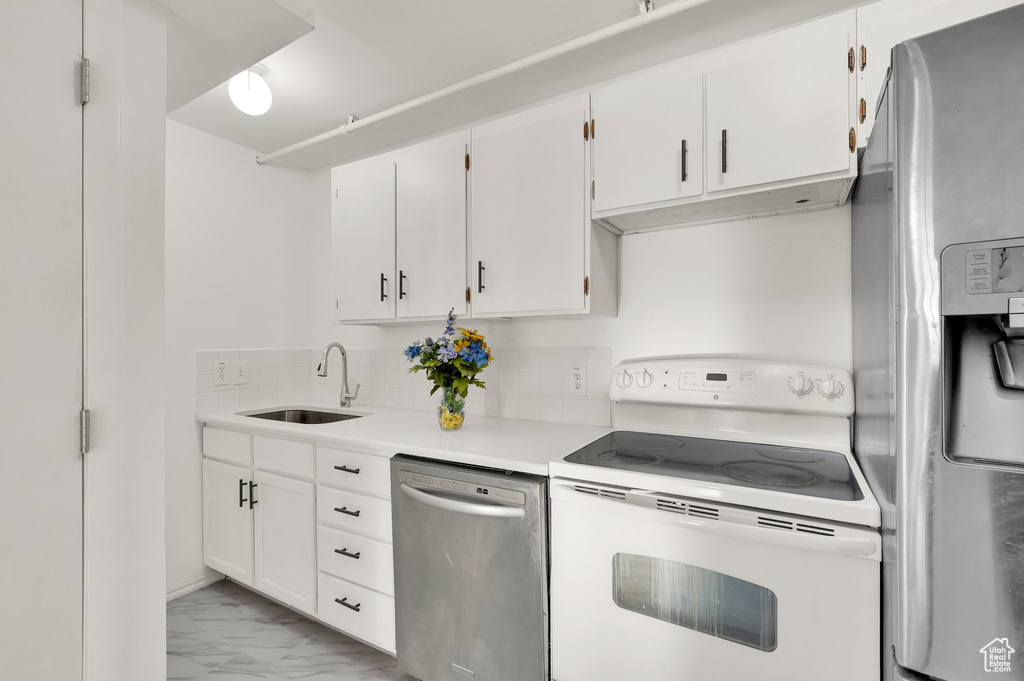 Kitchen with stainless steel appliances, light marble finish floors, decorative backsplash, white cabinets, and light countertops