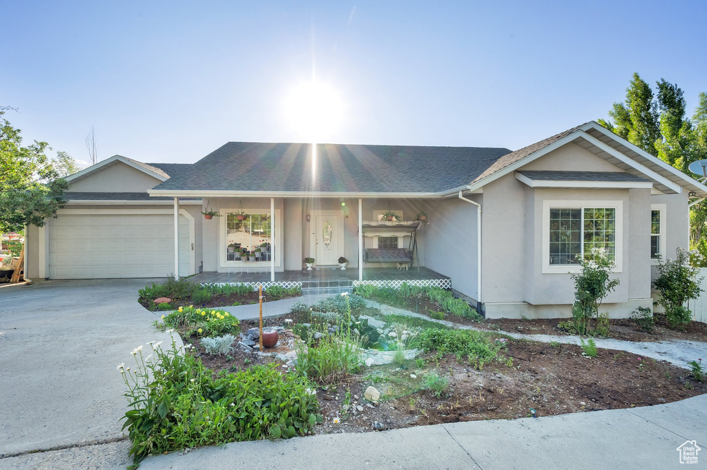 Ranch-style home with a garage, a porch, concrete driveway, stucco siding, and a shingled roof