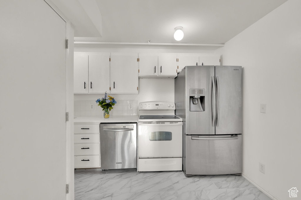 Kitchen featuring stainless steel appliances, light marble finish flooring, white cabinetry, light countertops, and backsplash