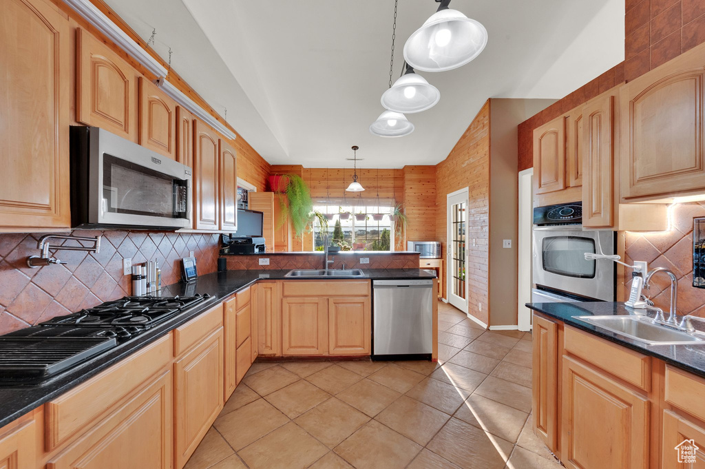 Kitchen with appliances with stainless steel finishes, a peninsula, decorative backsplash, light brown cabinets, and light tile patterned flooring