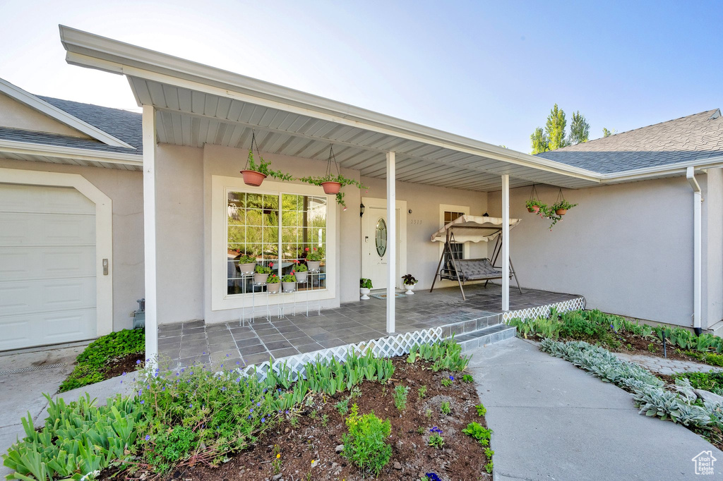 Property entrance featuring a porch, roof with shingles, stucco siding, and a garage