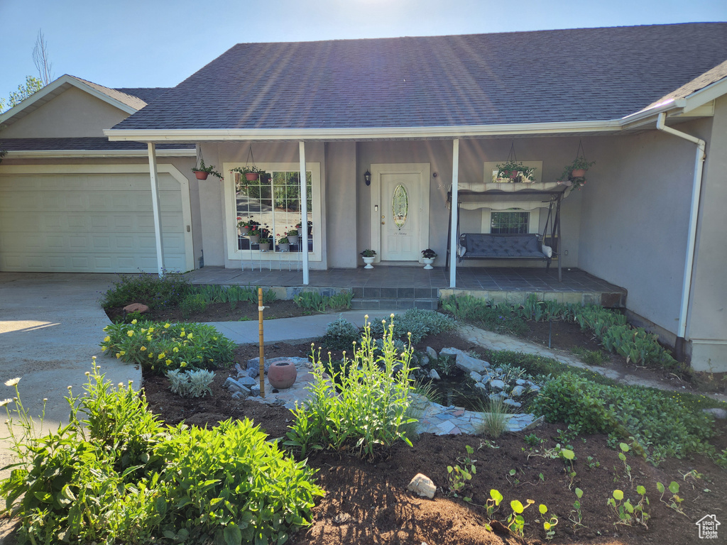 View of front of home with stucco siding, a porch, an attached garage, and roof with shingles