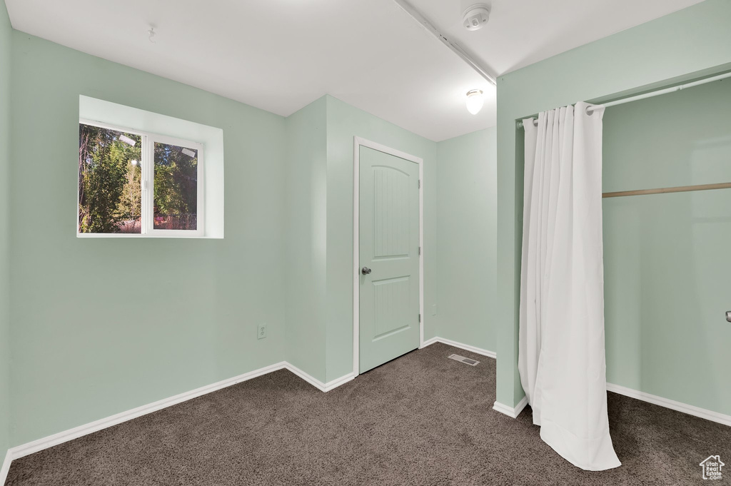 Unfurnished bedroom with dark carpet and baseboards