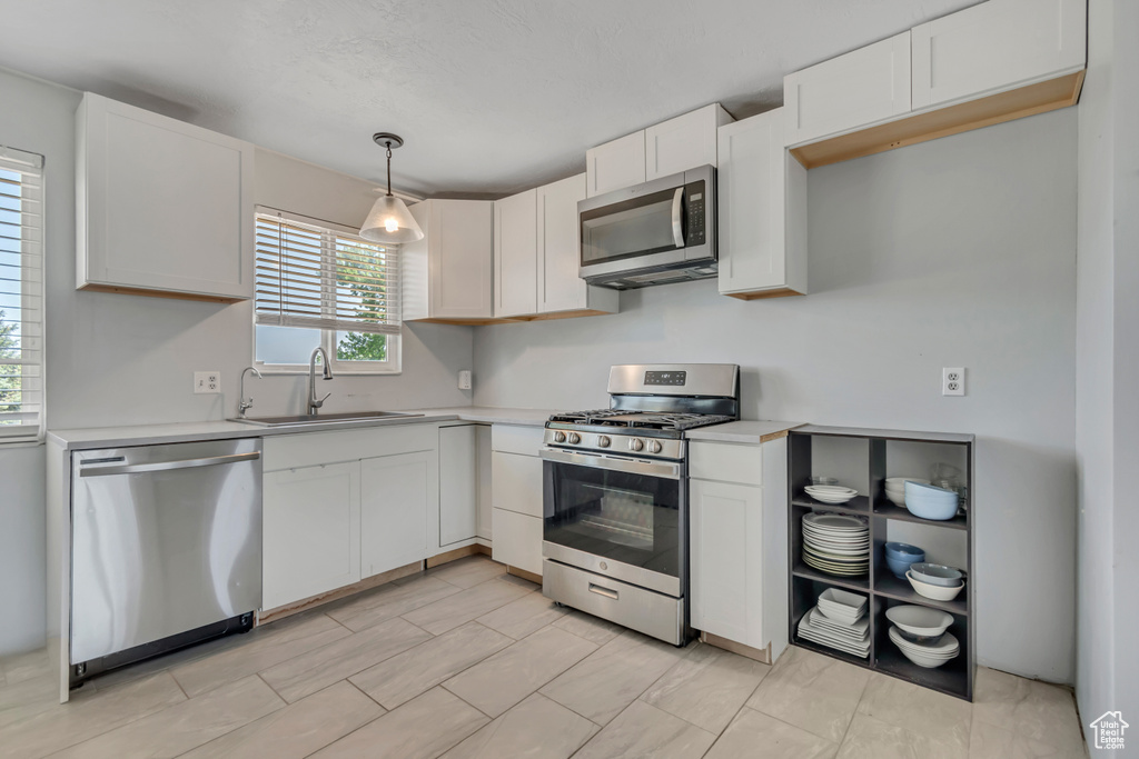 Kitchen with appliances with stainless steel finishes, light countertops, white cabinets, and decorative light fixtures