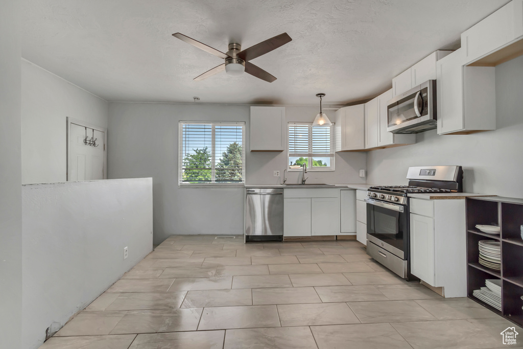 Kitchen featuring stainless steel appliances, a ceiling fan, white cabinets, decorative light fixtures, and light countertops