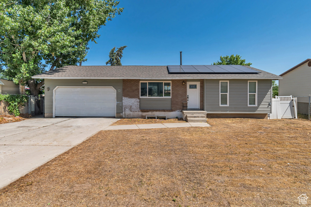 Single story home with a gate, roof mounted solar panels, an attached garage, concrete driveway, and brick siding