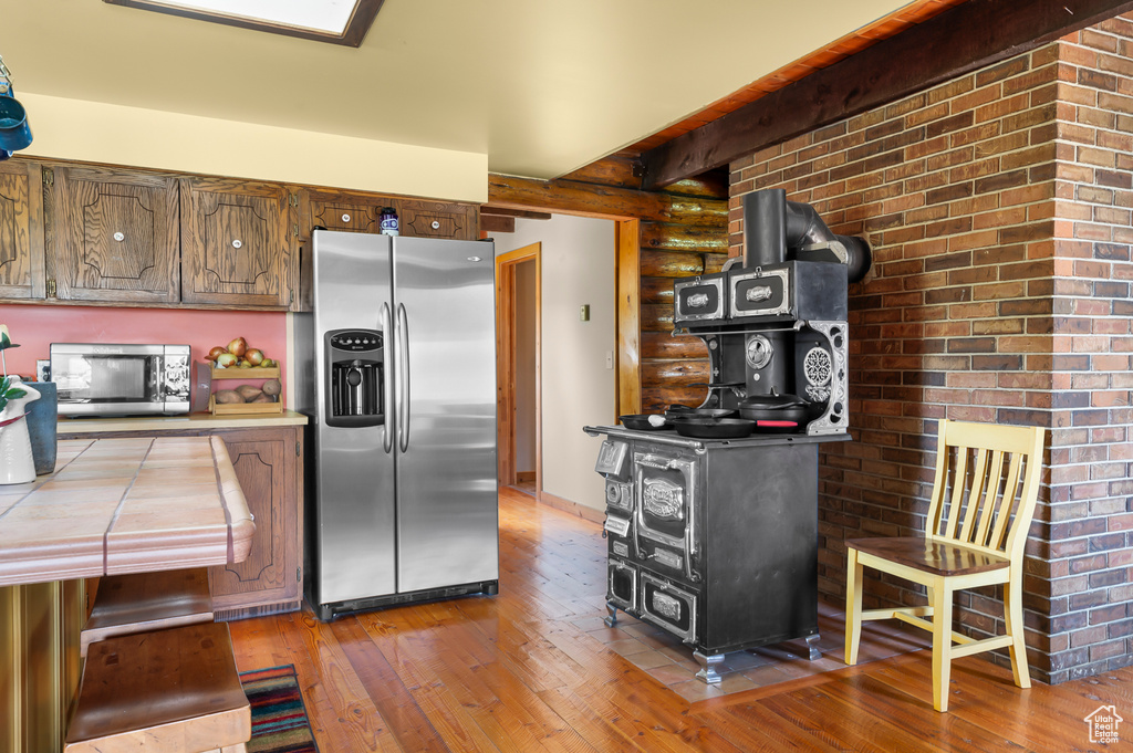 Kitchen featuring appliances with stainless steel finishes, rustic walls, a wood stove, wood-type flooring, and tile countertops