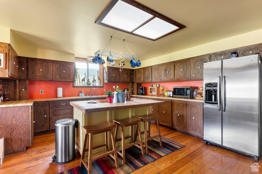 Kitchen featuring appliances with stainless steel finishes, tile countertops, a center island with sink, and light wood finished floors