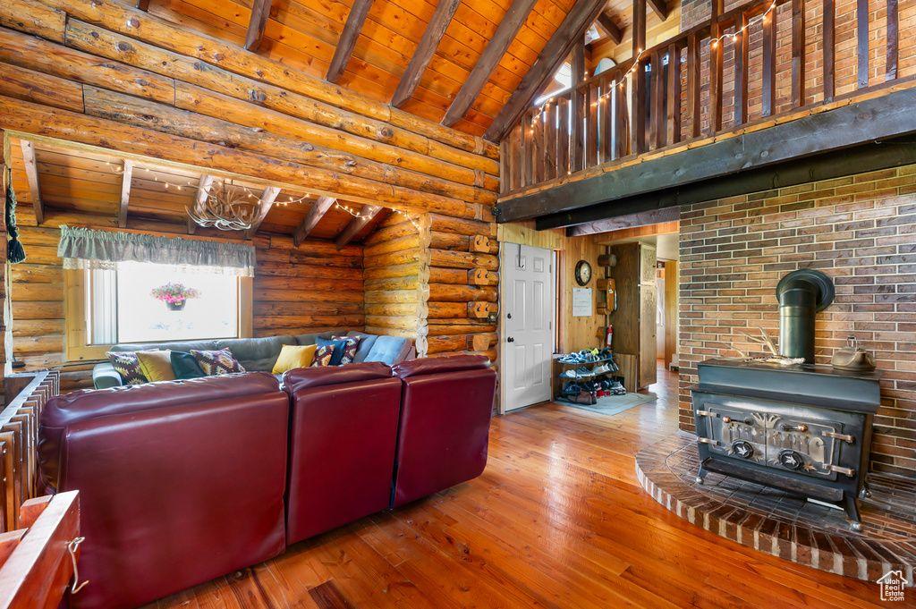 Living room with a wood ceiling with exposed beams, wood-type flooring, a wood stove, rustic walls, and high vaulted ceiling