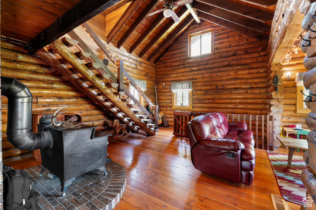 Living area featuring a wood stove, a wooden ceiling with exposed beams, wood-type flooring, high vaulted ceiling, and log walls