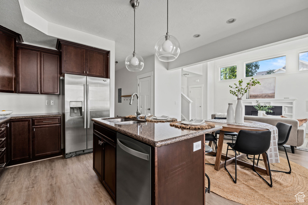 Kitchen with appliances with stainless steel finishes, dark stone counters, light wood-style flooring, dark brown cabinets, and a textured ceiling