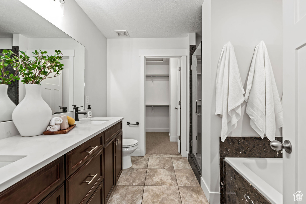 Bathroom featuring double vanity, a bath, a shower stall, a textured ceiling, and a walk in closet