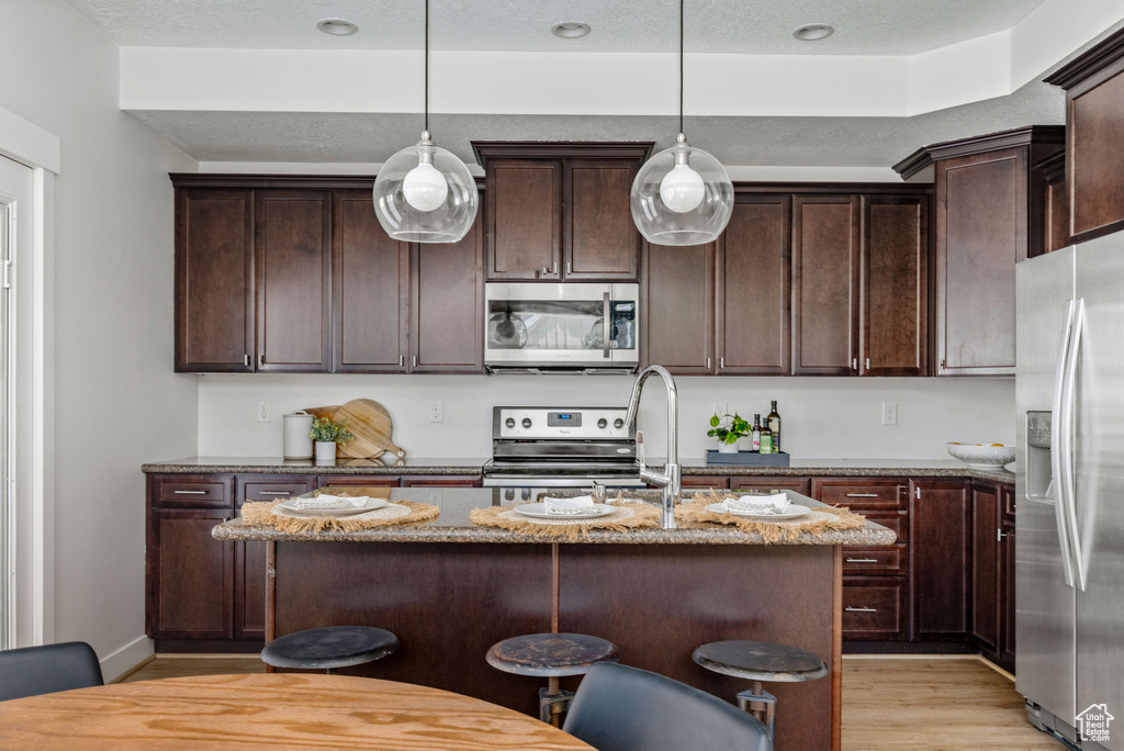 Kitchen featuring stainless steel appliances, light stone countertops, light wood finished floors, and an island with sink