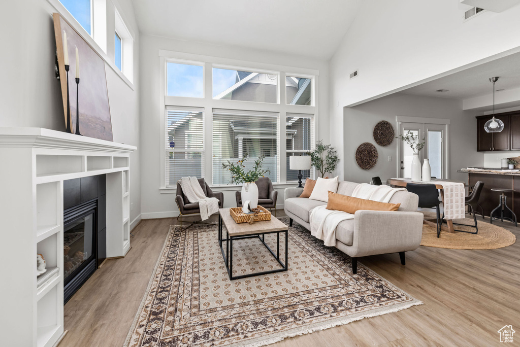 Living room featuring a glass covered fireplace, high vaulted ceiling, light wood-style flooring, and healthy amount of natural light