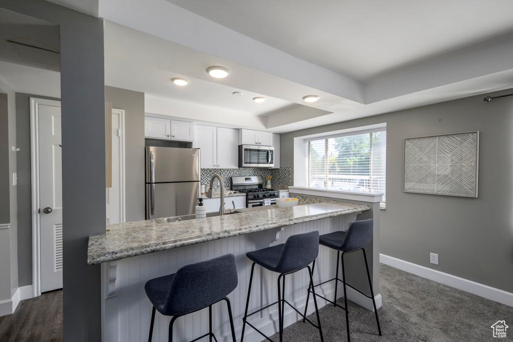 Kitchen with appliances with stainless steel finishes, white cabinets, a breakfast bar, a tray ceiling, and light stone countertops