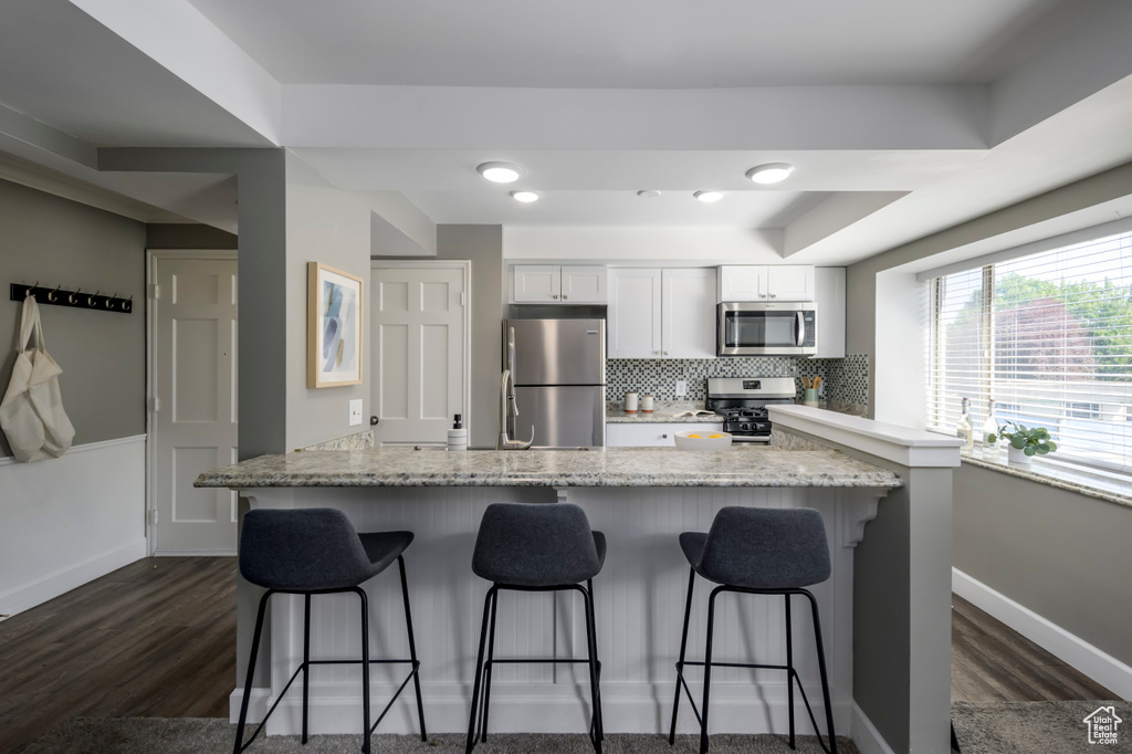 Kitchen with appliances with stainless steel finishes, a breakfast bar, dark wood-style flooring, and white cabinets
