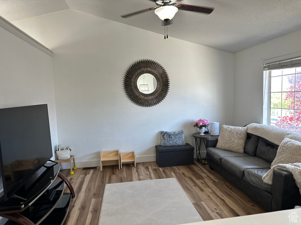 Living room featuring a ceiling fan, wood finished floors, and lofted ceiling