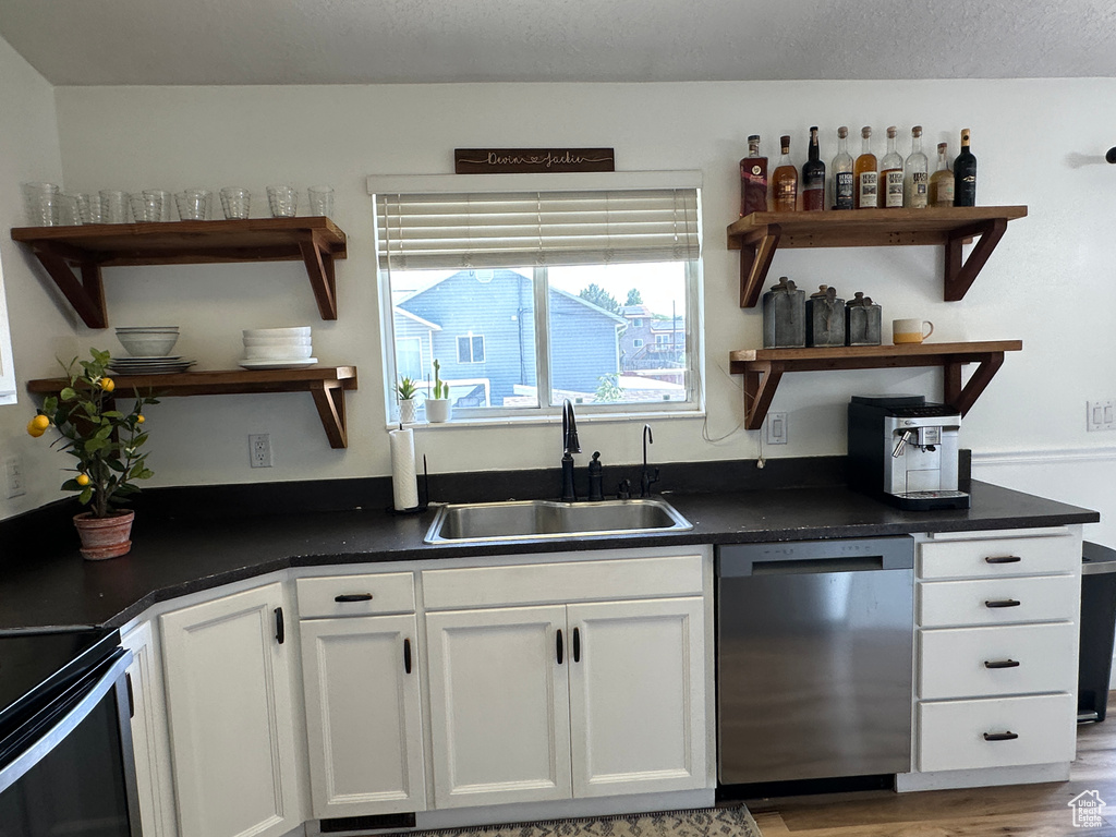Kitchen featuring open shelves, stainless steel dishwasher, white cabinets, dark countertops, and wood finished floors