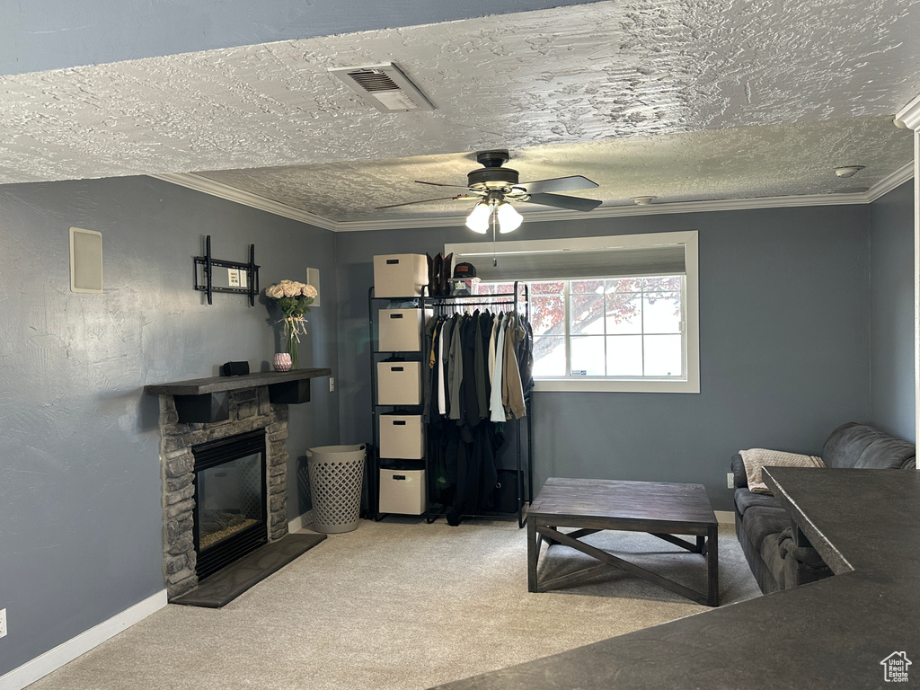 Carpeted bedroom featuring a stone fireplace, ornamental molding, a textured ceiling, and ceiling fan