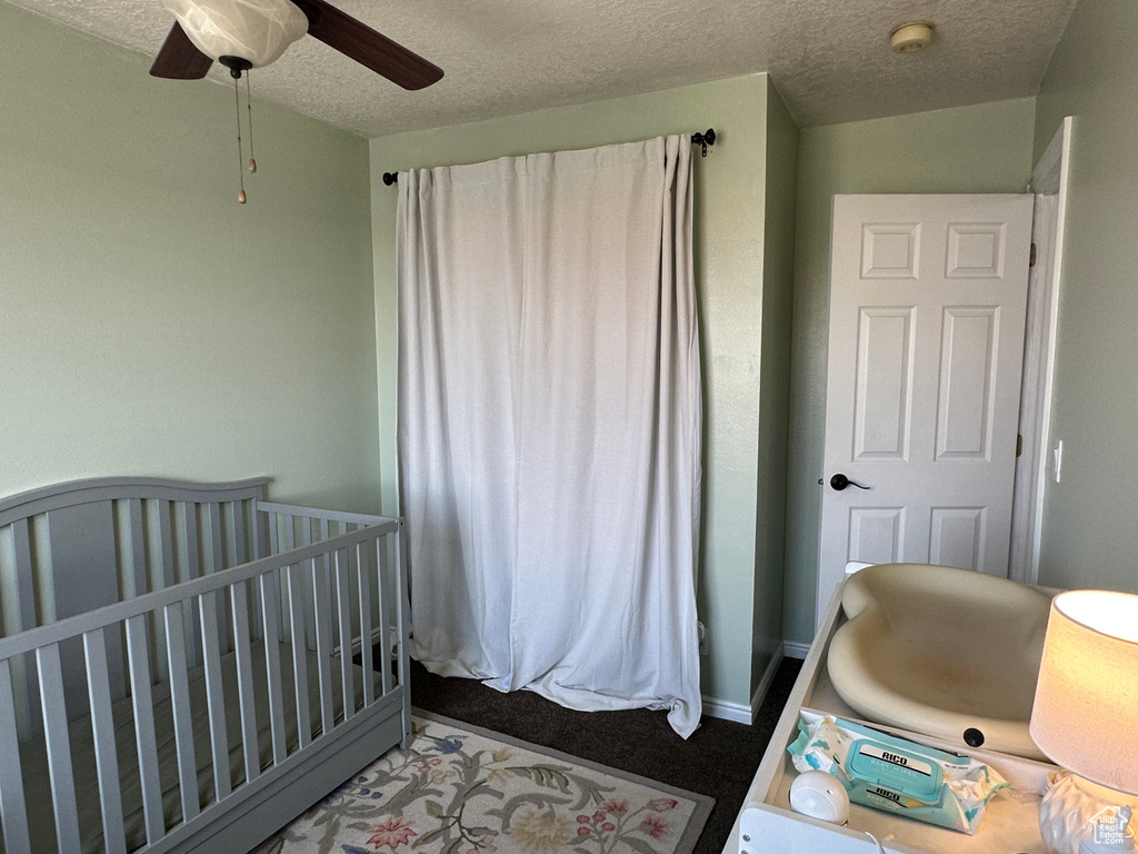 Bedroom with a crib, a textured ceiling, and a ceiling fan