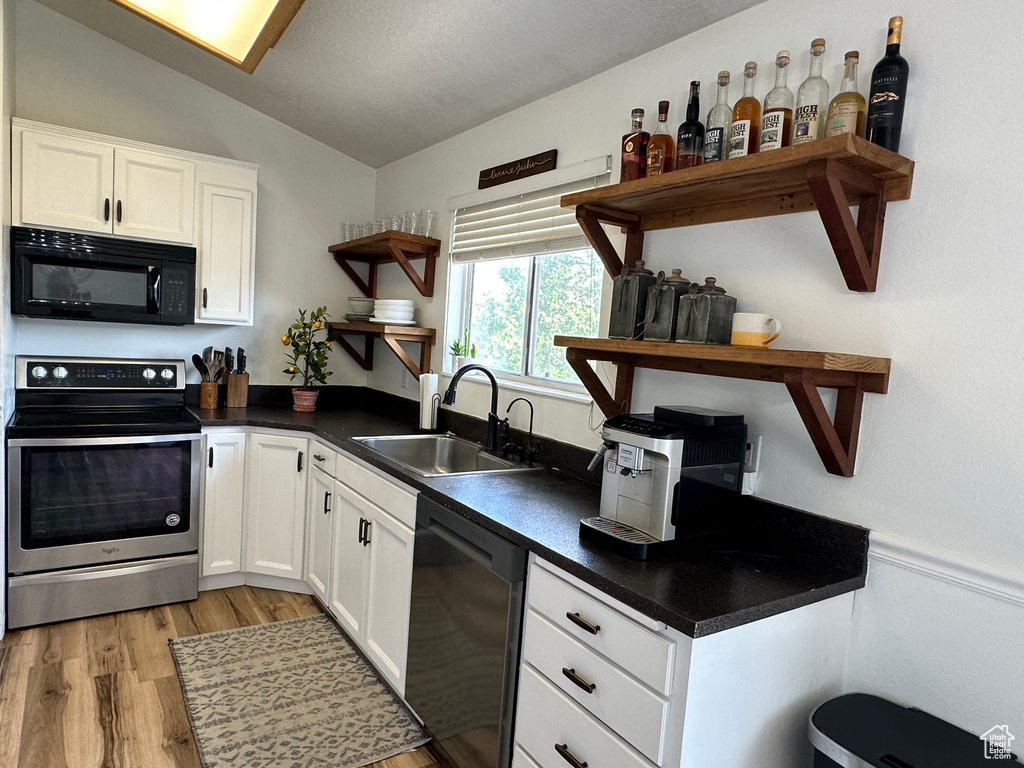 Kitchen with open shelves, black microwave, dishwashing machine, electric stove, and vaulted ceiling