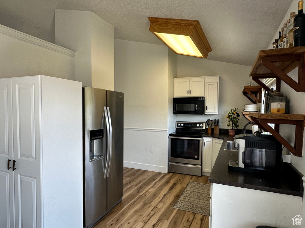 Kitchen with appliances with stainless steel finishes, dark countertops, light wood finished floors, white cabinets, and a textured ceiling