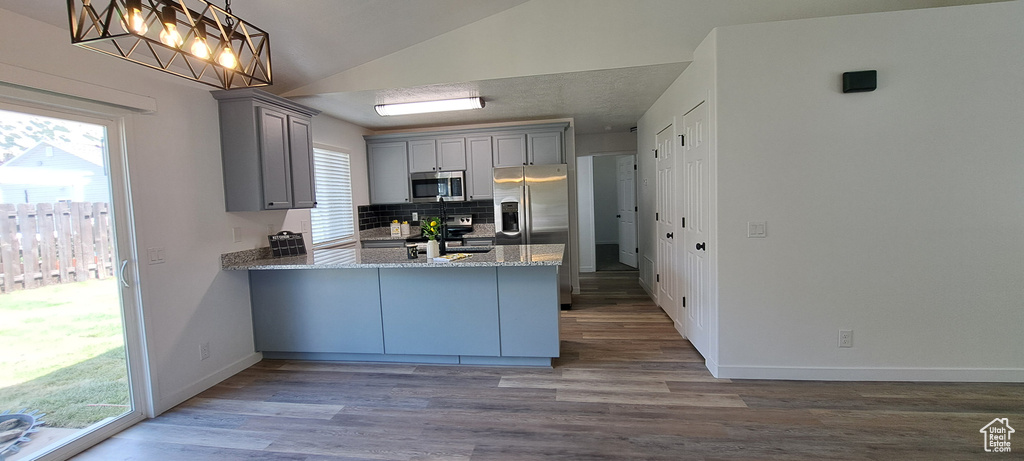 Kitchen with stainless steel appliances, gray cabinets, lofted ceiling, a peninsula, and wood finished floors