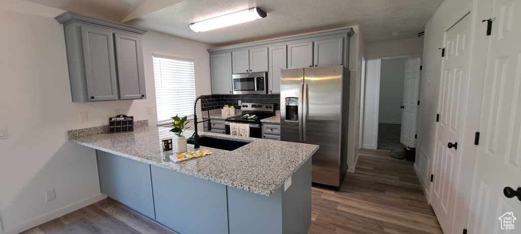 Kitchen with stainless steel appliances, gray cabinets, a peninsula, decorative backsplash, and a textured ceiling