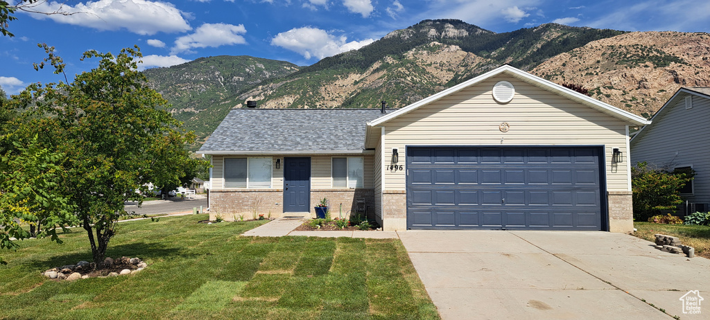 Single story home with a mountain view, a front yard, driveway, brick siding, and a garage