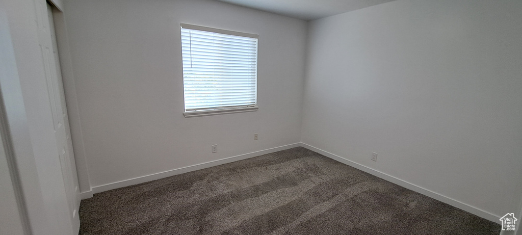 Empty room featuring dark colored carpet and baseboards
