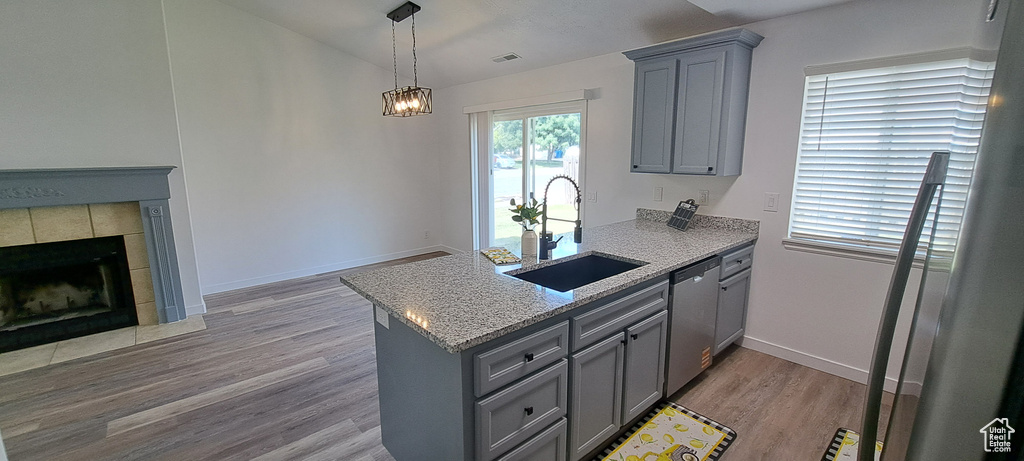 Kitchen with gray cabinetry, dishwasher, a peninsula, light wood-style flooring, and light stone countertops