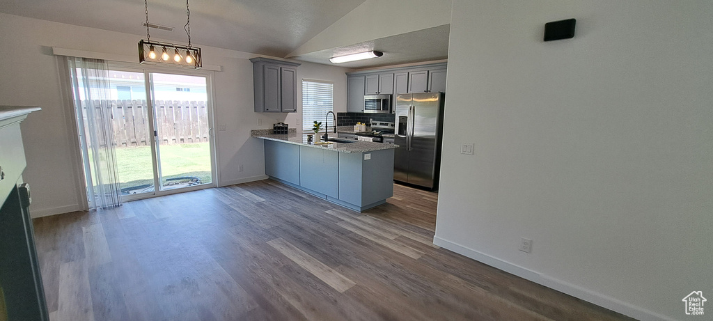 Kitchen with appliances with stainless steel finishes, gray cabinets, a peninsula, lofted ceiling, and backsplash