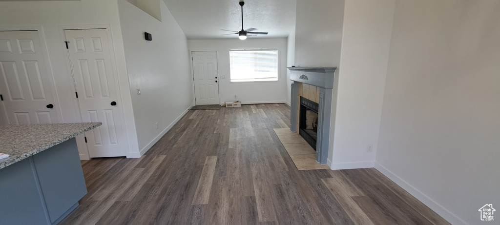 Unfurnished living room featuring a tiled fireplace, a ceiling fan, and dark wood-type flooring