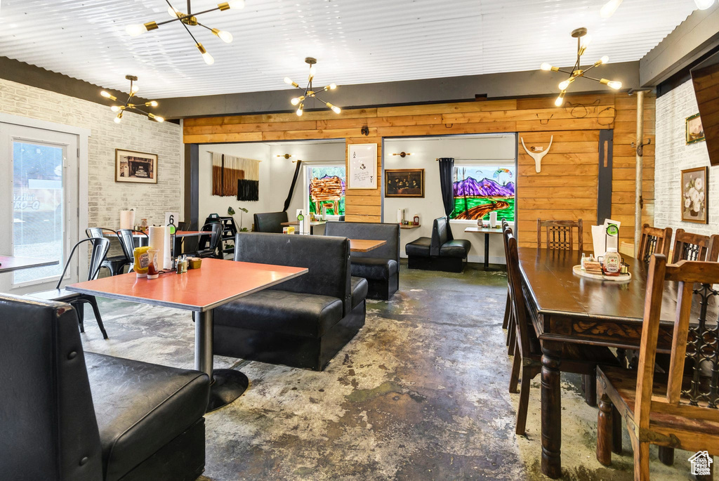 Dining space featuring a chandelier, concrete flooring, brick wall, and wood walls