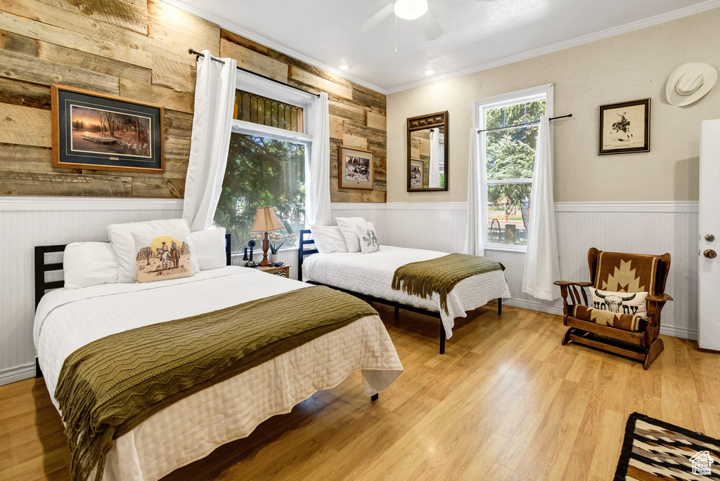 Bedroom featuring crown molding, wooden walls, wainscoting, wood finished floors, and ceiling fan