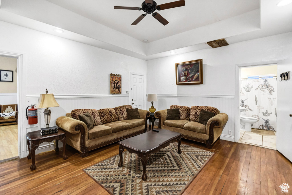 Living area featuring wood-type flooring, ceiling fan, a wainscoted wall, and a raised ceiling