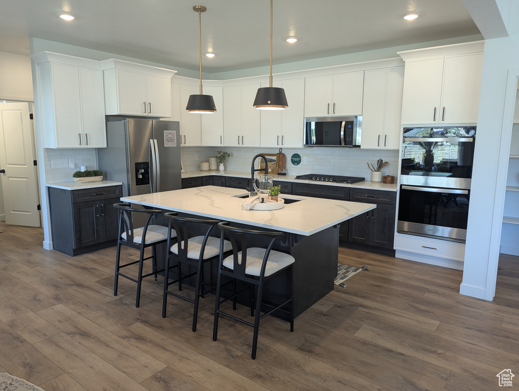 Kitchen with stainless steel appliances, dark wood finished floors, a kitchen bar, a center island with sink, and tasteful backsplash