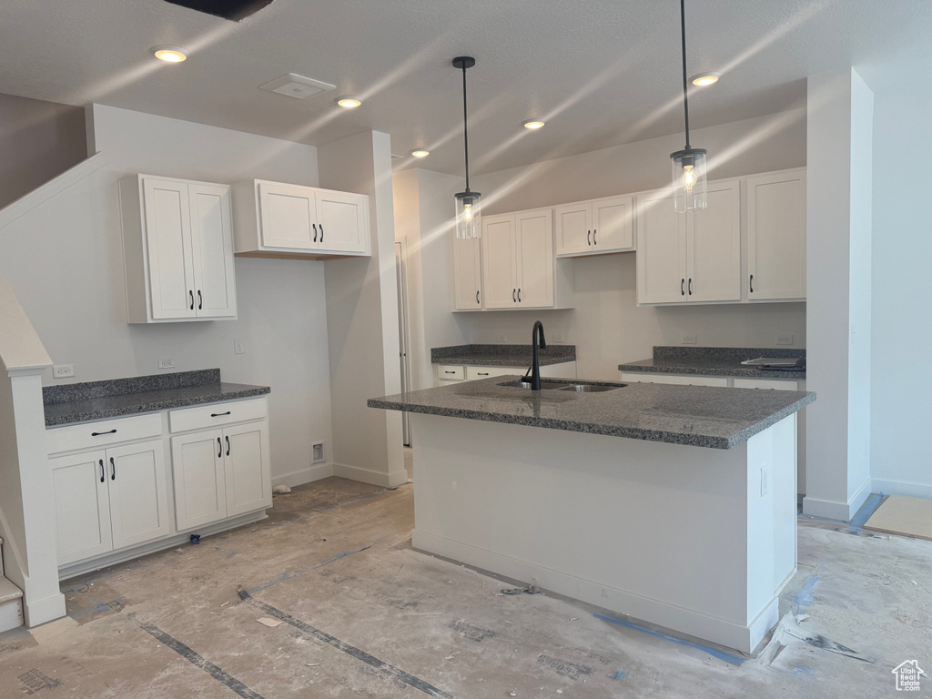 Kitchen featuring white cabinets, dark stone counters, a kitchen island with sink, decorative light fixtures, and recessed lighting