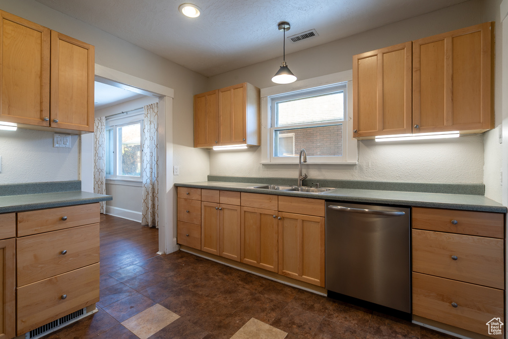 Kitchen featuring dishwasher, light brown cabinetry, decorative light fixtures, and dark countertops