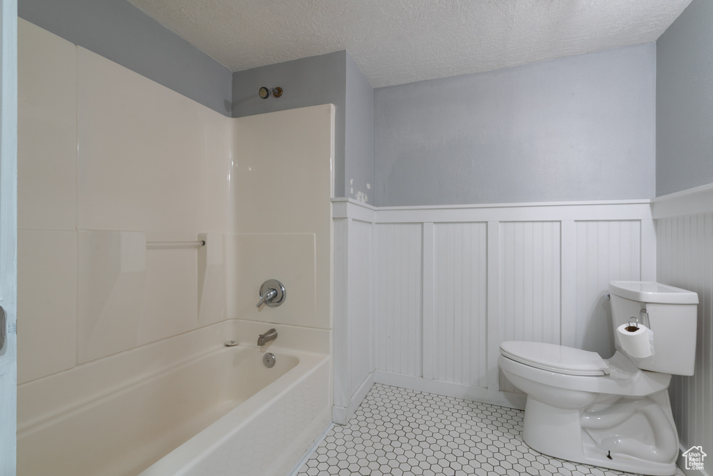 Full bathroom featuring a wainscoted wall, shower / bathtub combination, a decorative wall, and a textured ceiling