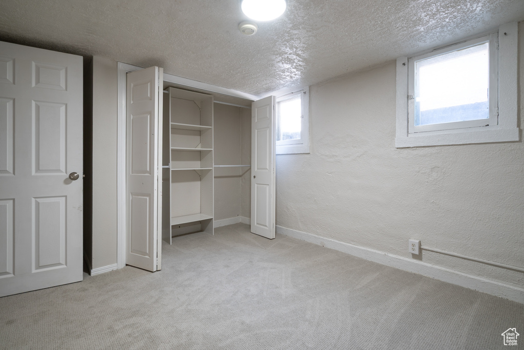 Unfurnished bedroom featuring a textured ceiling, light carpet, a textured wall, and a closet
